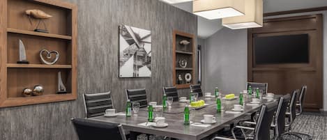 Un salón de conferencias con una mesa larga, sillas y estanterías con adornos.