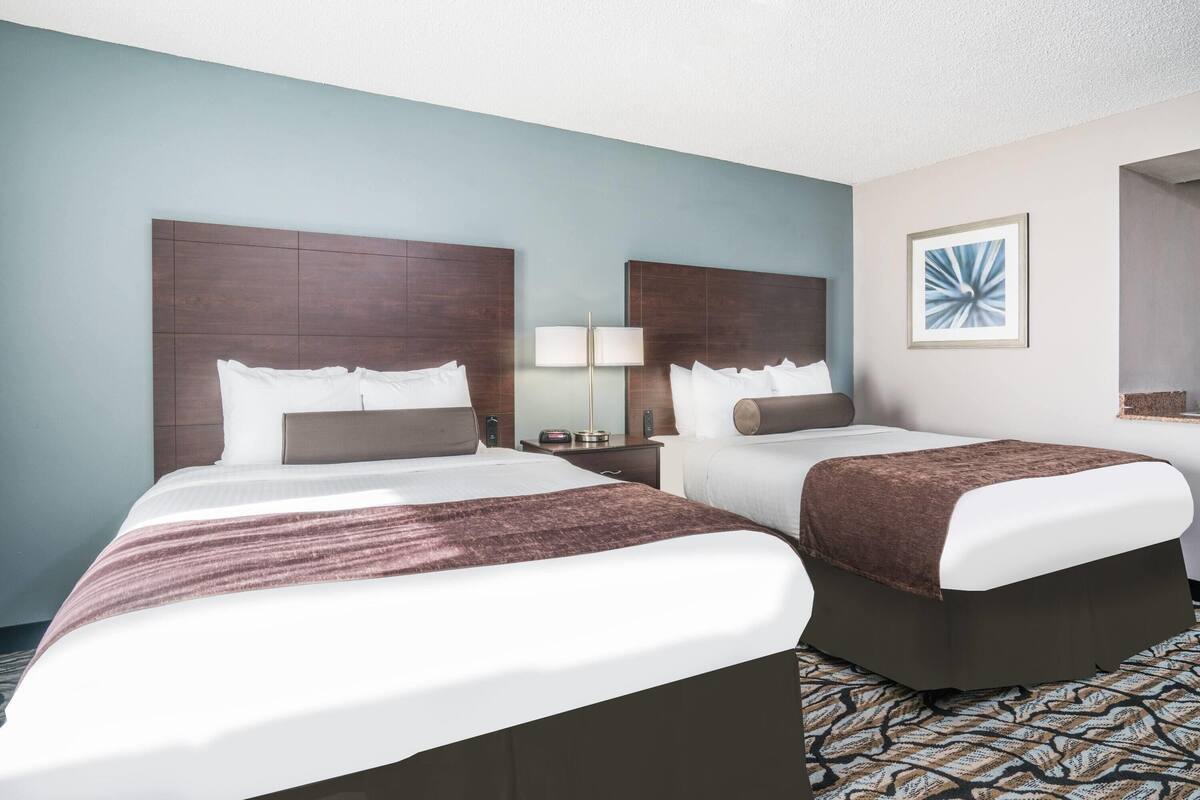 A hotel room with two beds, a nightstand, a lamp, and a framed picture on the wall.