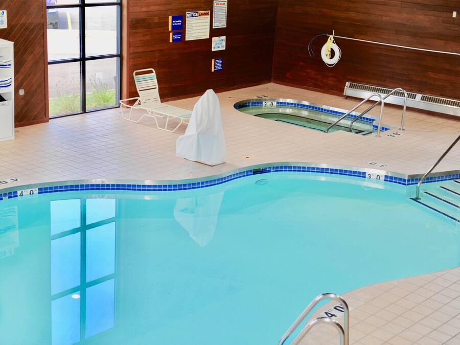 An indoor swimming pool with a tiled edge, a lounge chair, and a small hot tub.
