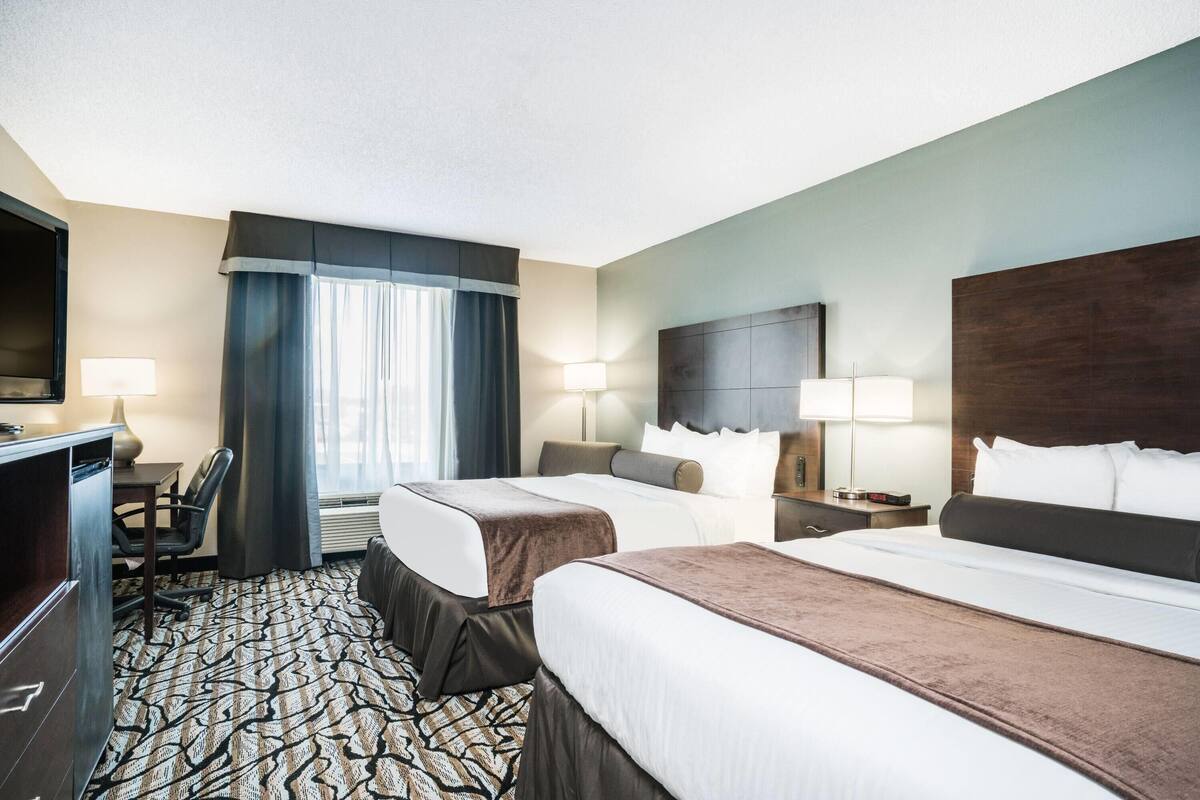 A hotel room with two beds, a desk, and a TV.