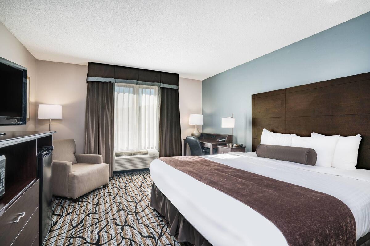 A hotel room with a large bed, a desk, a chair, a TV, and a window with curtains.
