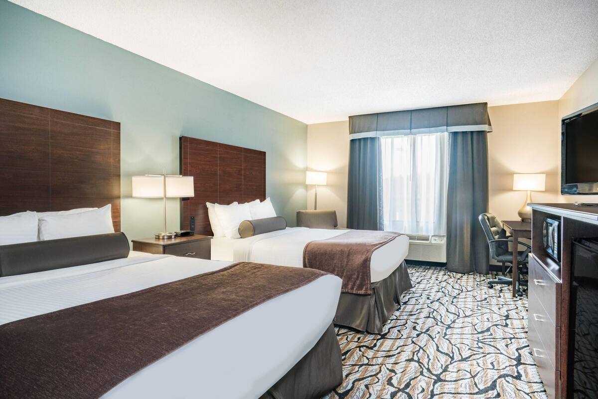 A hotel room with two beds, a desk, a TV, and a window with curtains.