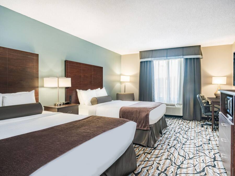 A hotel room with two beds, a desk, a TV, and a window with curtains.