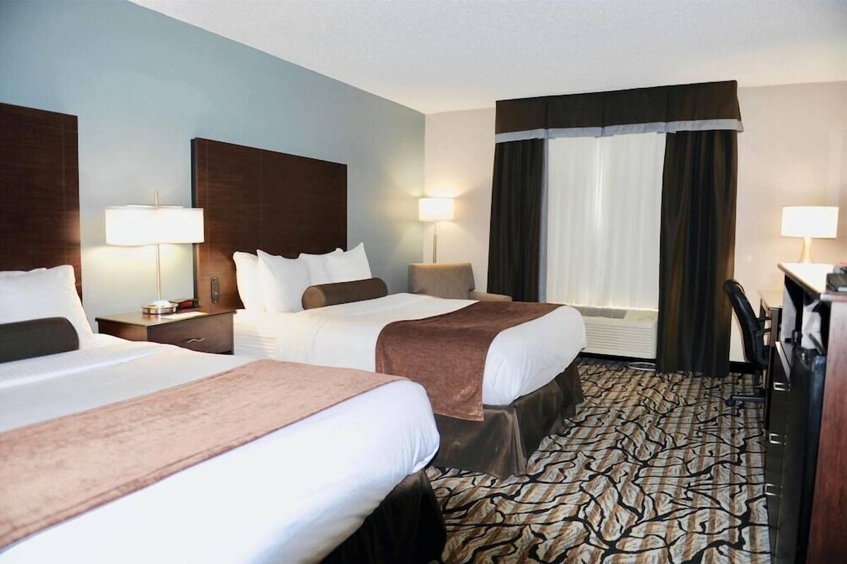 A hotel room with two beds, a desk, a chair, and a large window with curtains.