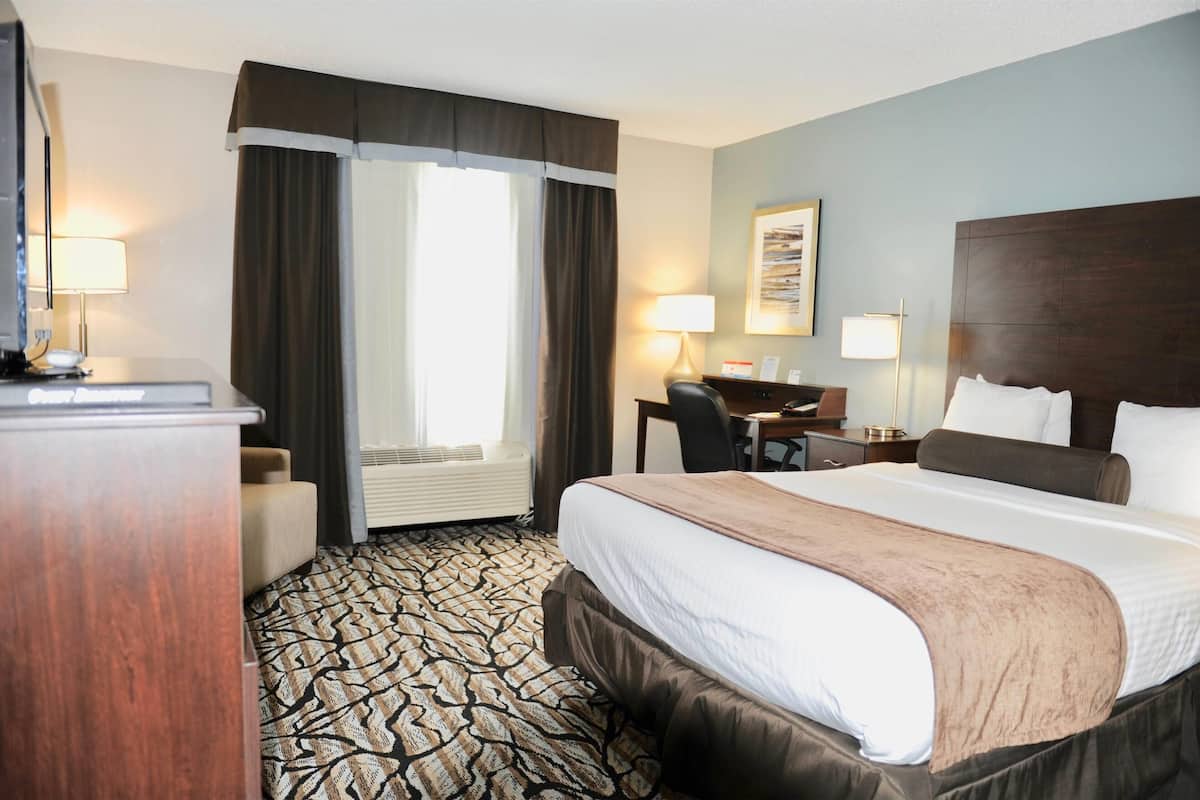 A hotel room with a large bed, a desk, a chair, a desk lamp, and a window with curtains.