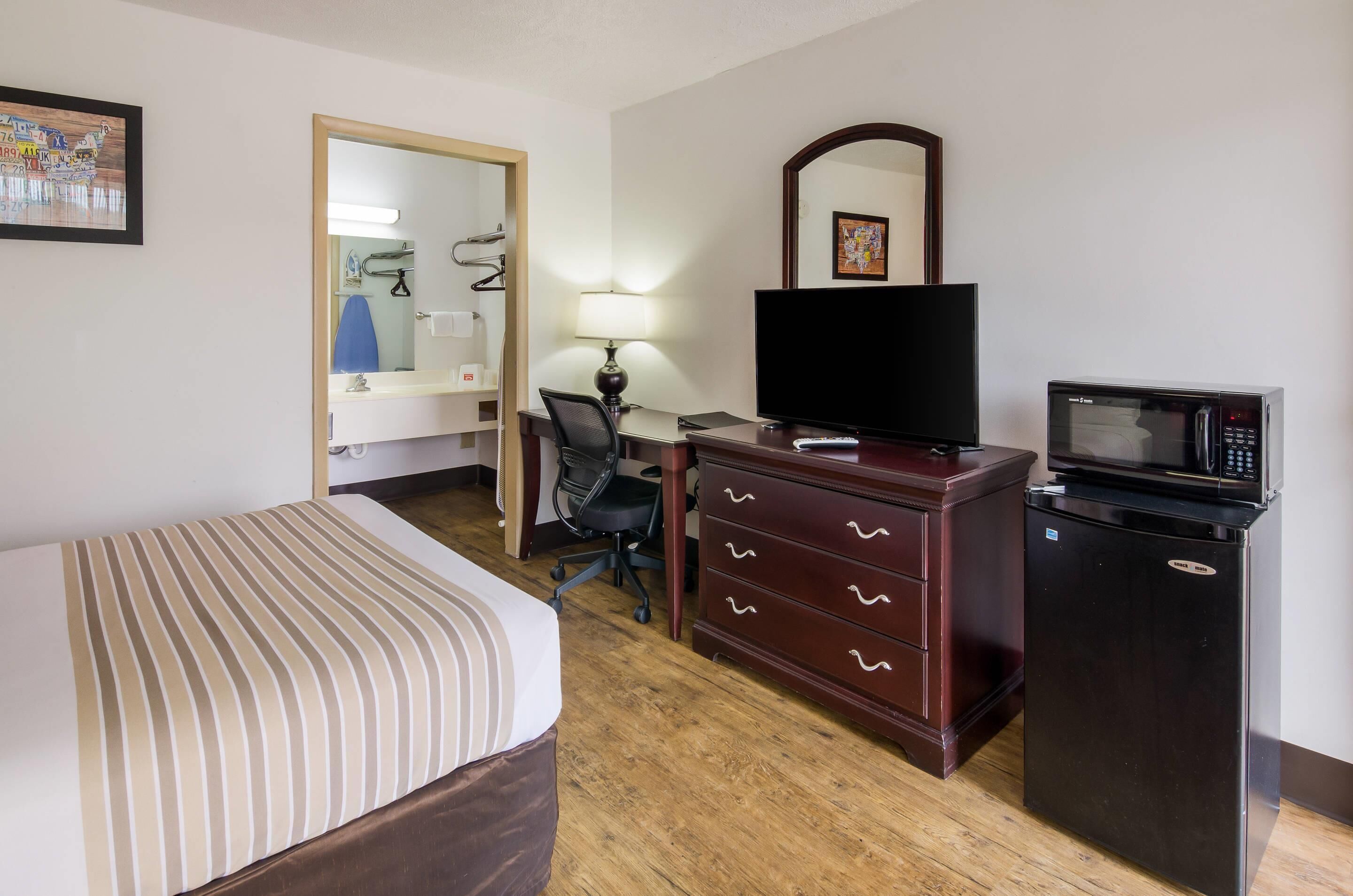 A hotel room with a bed, a desk with a chair, a television, a microwave, and a dresser.