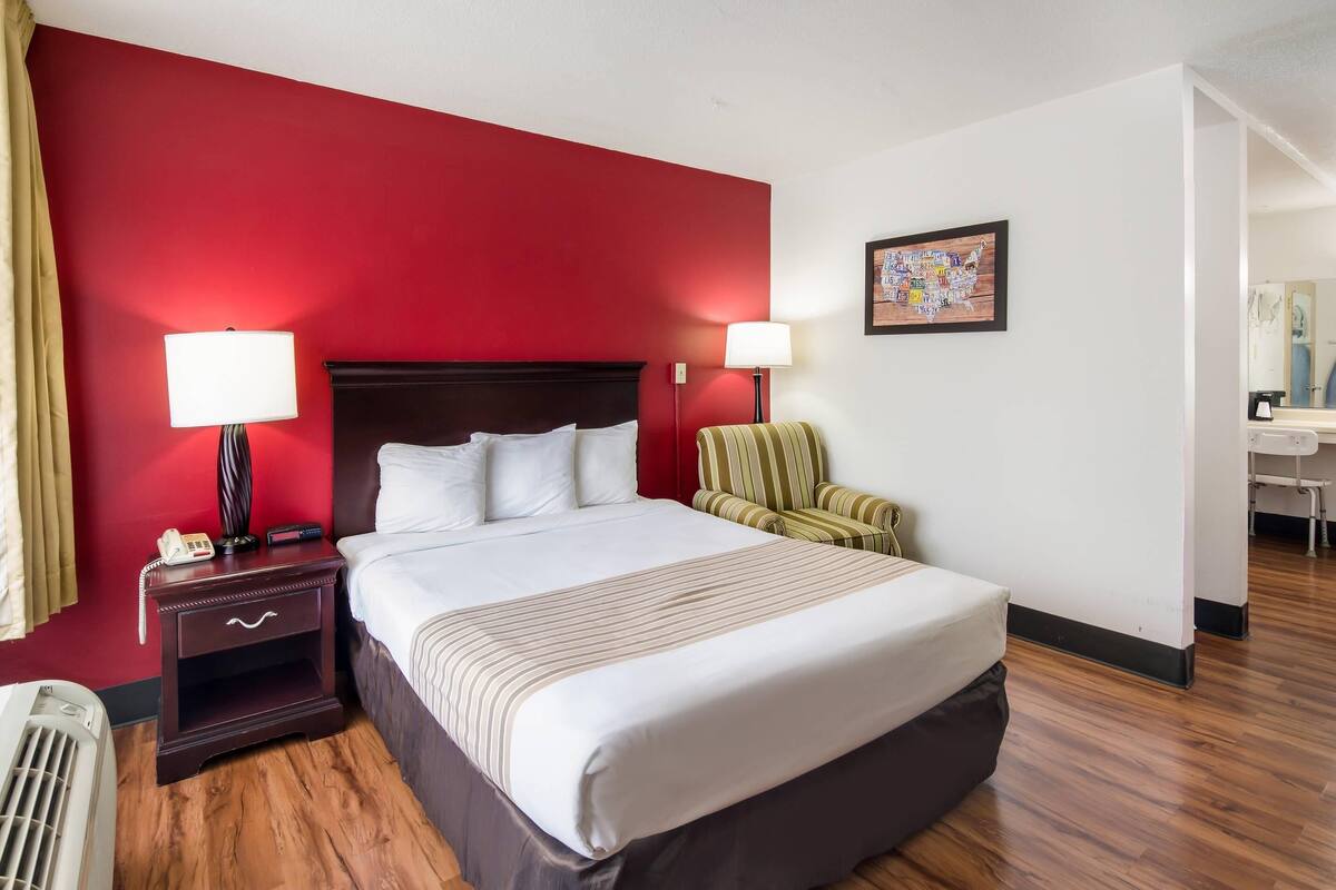 Habitación de hotel con una cama grande, dos lámparas de noche, una silla, una mesita y un cuadro en la pared.