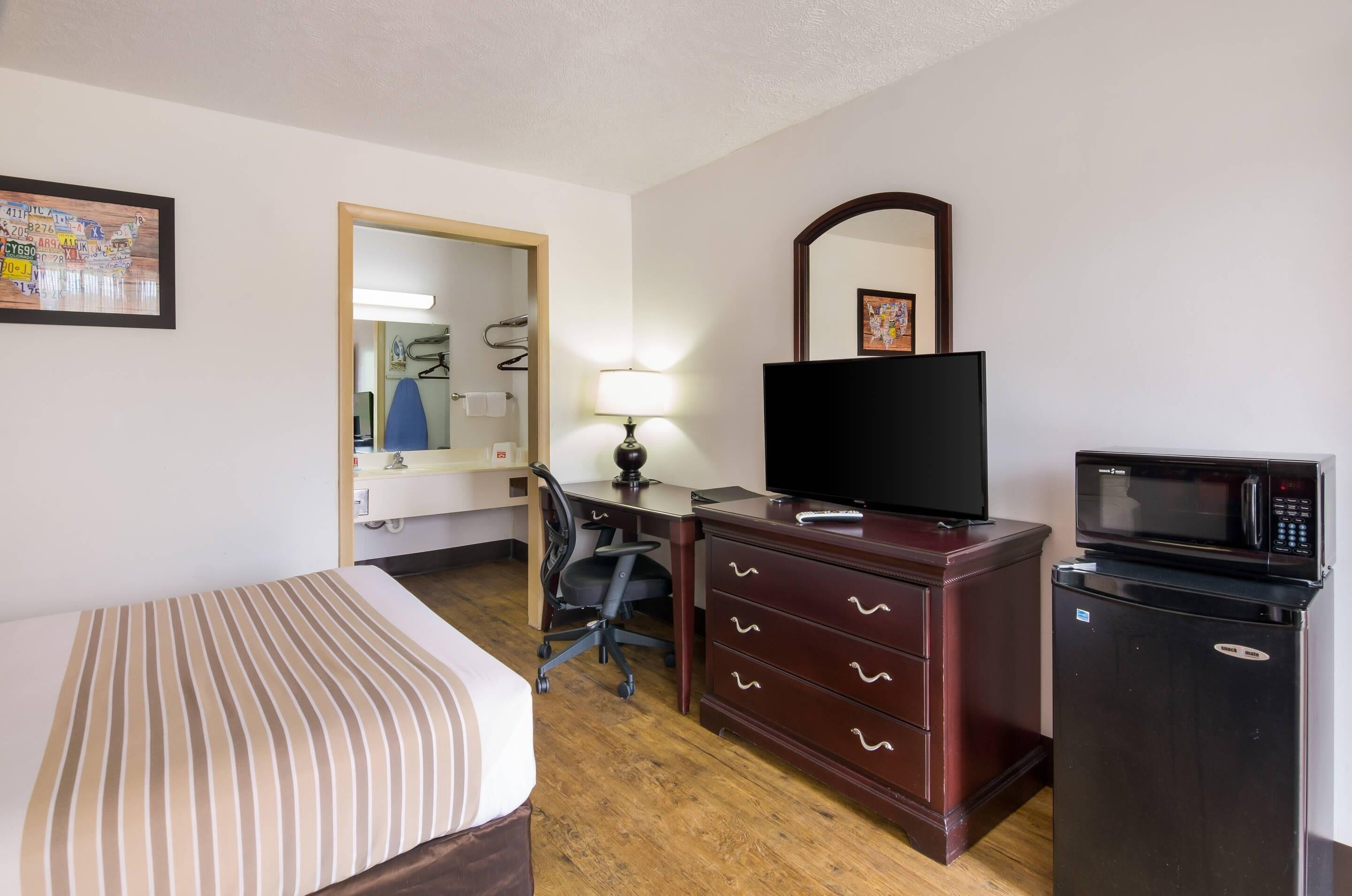 A hotel room with a bed, a desk, a chair, a television, a microwave, and a dresser.