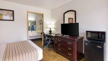 A hotel room with a bed, a desk, a chair, a television, a microwave, and a dresser.
