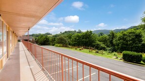 A balcony with a view of a road and greenery, a building with a red railing, and a clear blue sky.