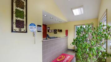 Et hotellets receptionområde med reception, en sikkerhedsadvarsel, indrammede certifikater og en rød dørmåtte.