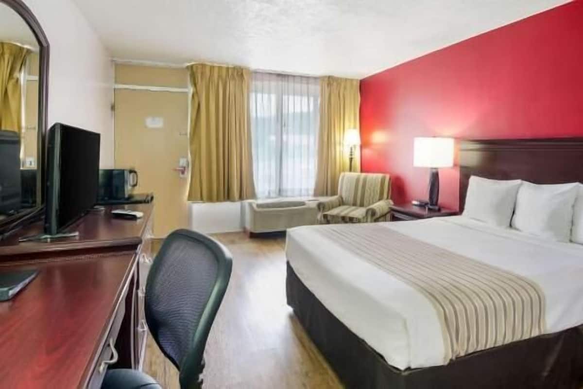 Habitación de hotel con cama, escritorio con computadora, silla, televisor y ventana con cortinas.