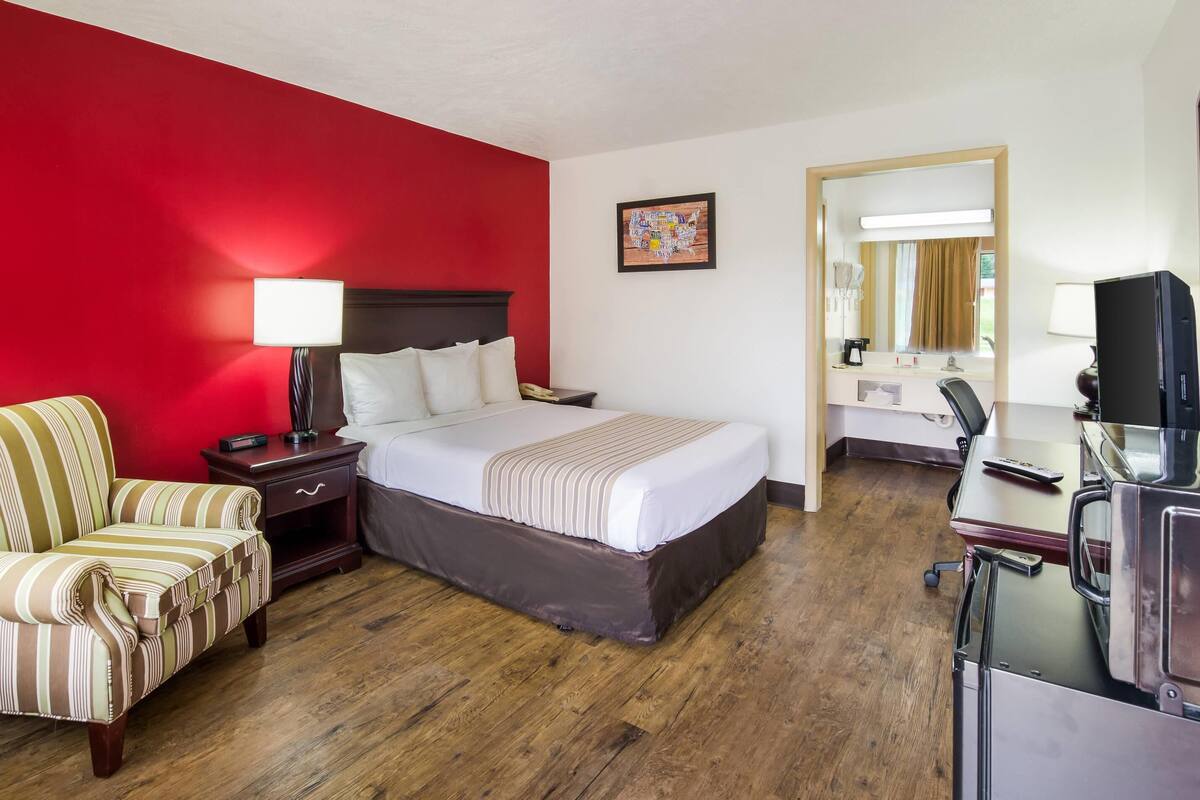 Una habitación de hotel con cama, una silla, escritorio y televisor.