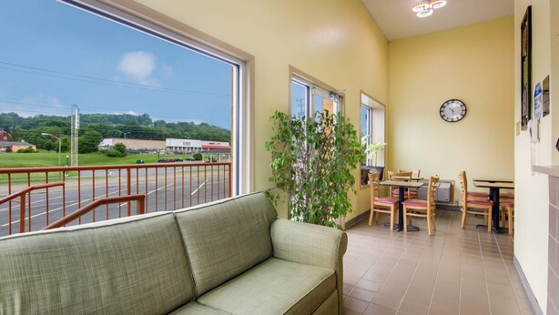 A hotel room with a balcony, a sofa, a dining area with chairs and tables, and a clock on the wall.