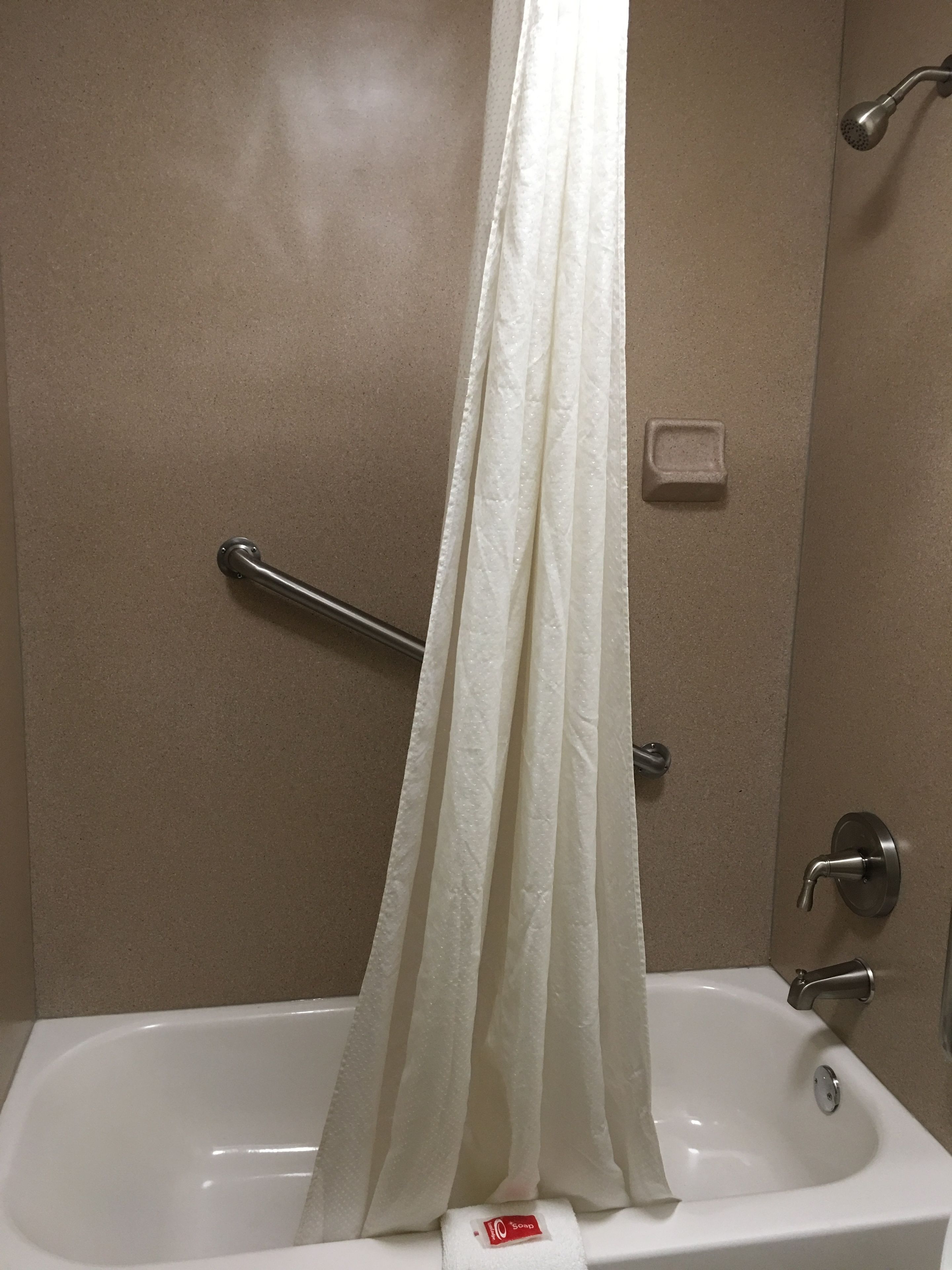 Un baño con bañera, cortina de ducha, barra de apoyo y dispensador de jabón.