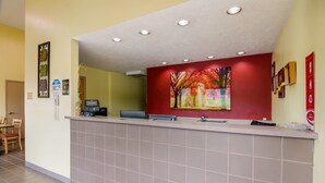 A reception area with a counter, a painting of autumn trees, a desk with a computer, and a chair.