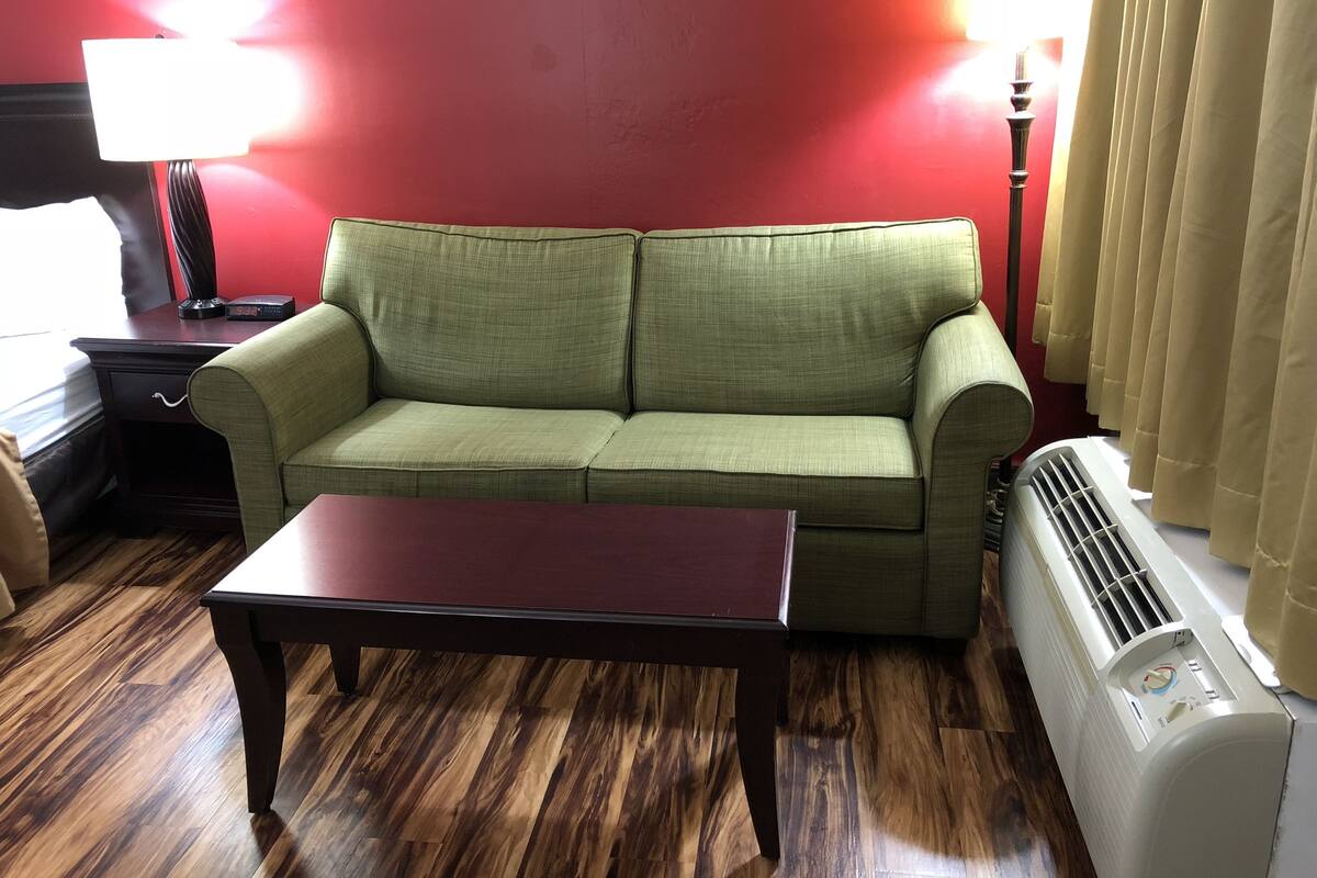 Una sala de estar con un sofá verde, una mesa de centro de madera oscura, una pared roja, una lámpara y un radiador blanco.