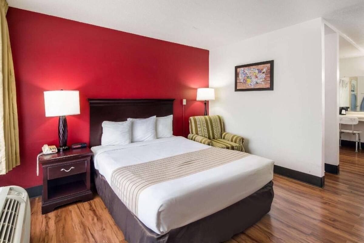 Una habitación de hotel con una cama grande, dos lámparas de noche, una silla, un escritorio y un espejo.