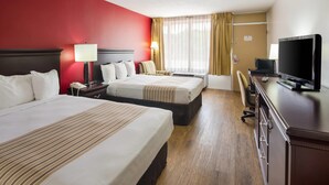 A hotel room with two beds, a desk with a TV, a lamp, and a chair.