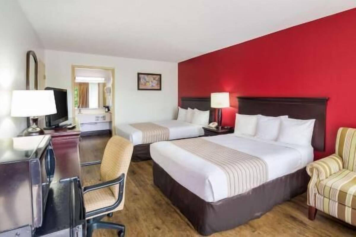 Habitación de hotel con dos camas, un escritorio con computadora, una silla y una pared de acento roja.