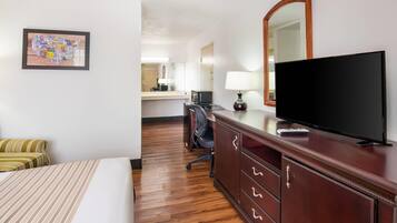 A hotel room with a bed, a desk with a television, a mirror, and a wall-mounted picture.
