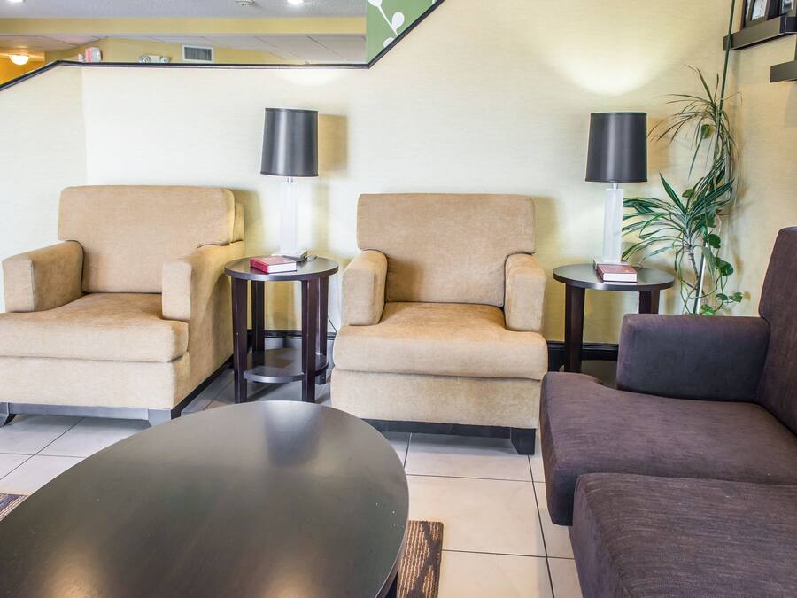 Eine Hotelhalle mit zwei beigen Sesseln, einem dunkelbraunen Sofa und einem runden Tisch. Es befinden sich zwei kleine Beistelltische mit Lampen und Büchern dort. Im Hintergrund ist eine Topfpflanze zu sehen.
