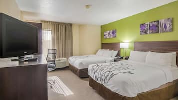 A hotel room with two beds, a TV, a desk, and a window with curtains.