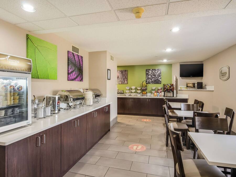 A modern kitchen with a refrigerator, microwave, and coffee machine. There are dining tables and chairs, and artwork on the walls.
