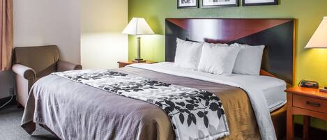 A hotel room with a large bed, a chair, a nightstand with a lamp, and framed pictures on the wall.