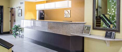 A reception area with a counter, a sign reading "Sleep Inn," a framed mirror, and a staircase in the background.
