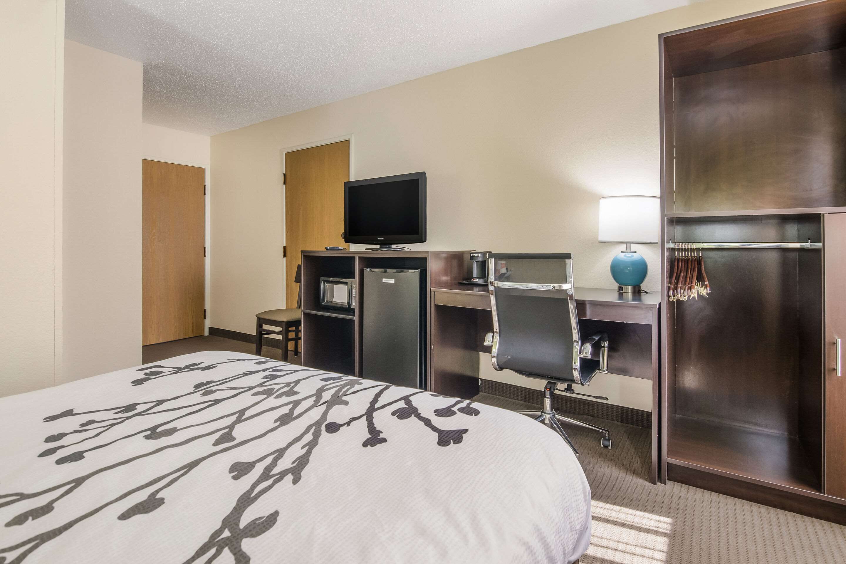 A hotel room with a large bed, a desk with a computer, a television, and a wardrobe.