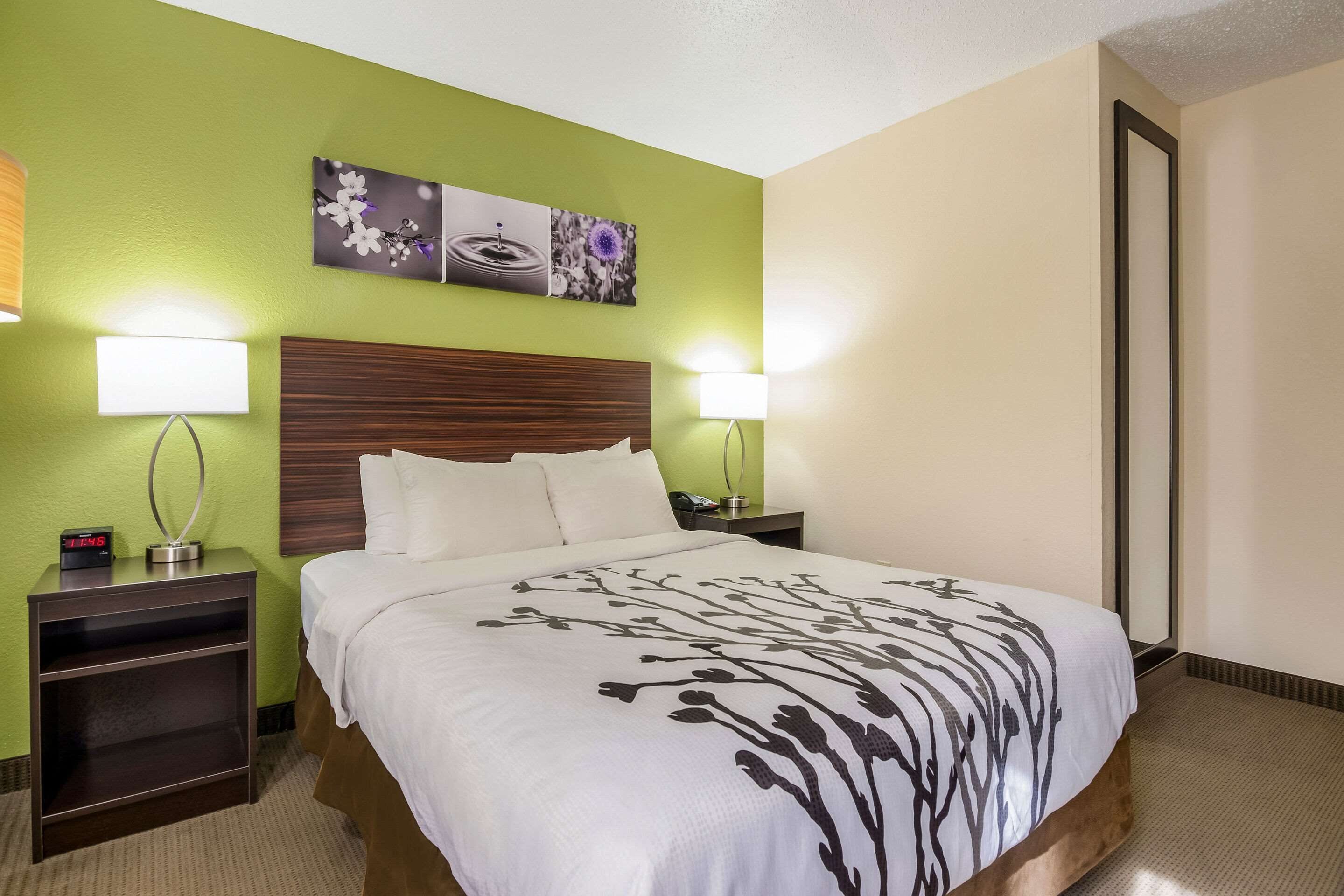 A hotel room with a large bed, two bedside tables with lamps, a wooden headboard, and two wall-mounted artworks.