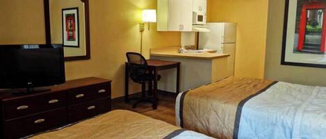 A hotel room with two beds, a desk, a television, and a refrigerator.