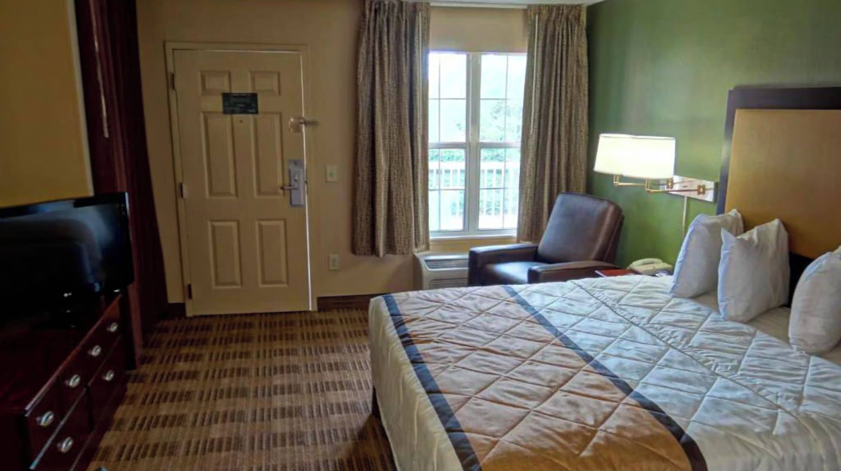 A hotel room with a bed, a TV, a chair, a desk, and a window with curtains.