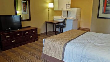 A hotel room with a bed, a TV, a desk with a chair, a microwave, and a refrigerator.