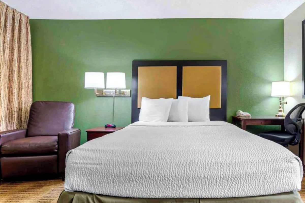 Una habitación de hotel con una cama grande, un sillón de cuero marrón, una mesita de noche y un escritorio con una lámpara.