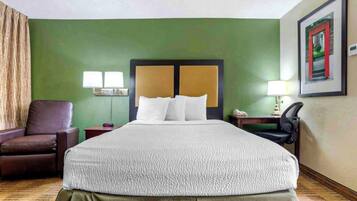 A hotel room with a large bed, a brown leather chair, a nightstand, and a desk with a lamp.