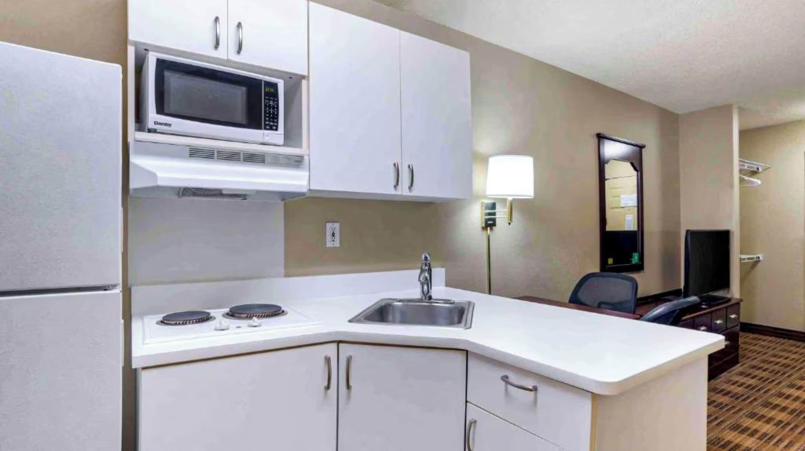 Cocina compacta de hotel con microondas, estufa, fregadero y armarios.