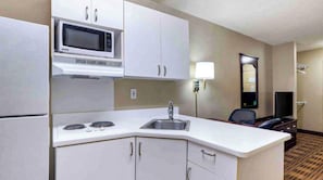 A compact hotel kitchenette with a microwave, stove, sink, and cabinets. - Studio 6 Extended Stay Huntsville, AL - US Space & Rocket Center (Huntsville)