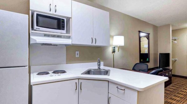 A compact hotel kitchenette with a microwave, stove, sink, and cabinets.