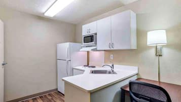 A compact kitchen with white cabinets, a microwave, a refrigerator, a sink, and a chair.