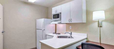 A compact kitchen with white cabinets, a microwave, a refrigerator, a sink, and a chair.