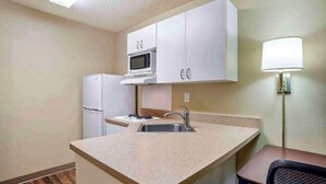 A compact kitchen with a microwave, refrigerator, sink, and a small dining area with a chair. - Studio 6 Extended Stay Huntsville, AL - US Space & Rocket Center (Huntsville)