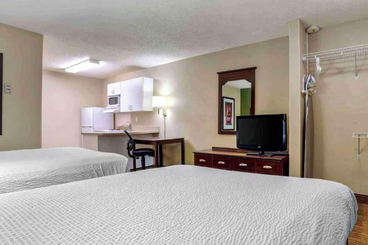 Habitación de hotel con dos camas, un escritorio, televisor, microondas y una pequeña kitchenette.