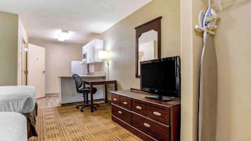Una habitación de hotel con cama, escritorio, silla, televisor, cómoda y microondas.