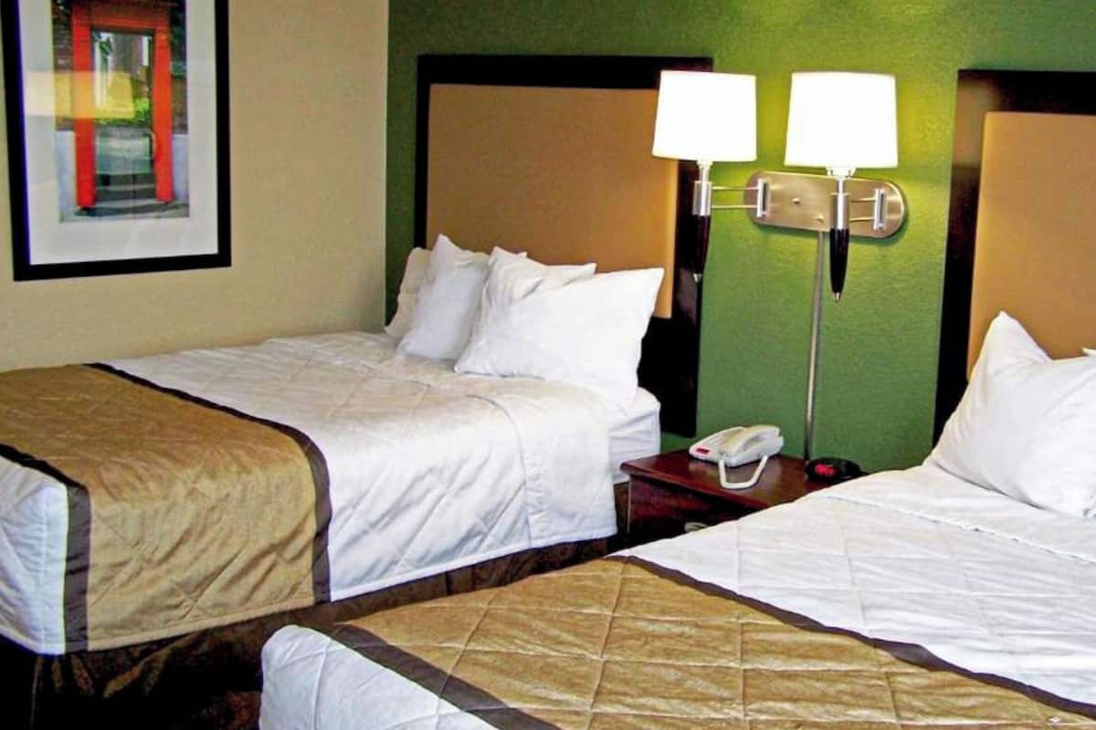 Habitación de hotel con dos camas, una mesita de noche, un teléfono y una lámpara fijada a la pared.