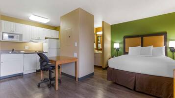 A hotel room with a bed, a desk with a chair, a kitchenette, and a bathroom.