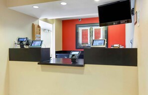 A reception area with two reception desks, a mounted television, and a window with a red door. - Extended Stay America Suites Phoenix Scottsdale (Scottsdale)
