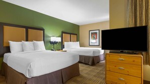 A hotel room with two beds, a television, a dresser, and a framed picture on the wall.