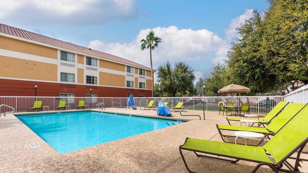 A swimming pool with lounge chairs and umbrellas, surrounded by a fence and trees.